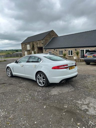 A white luxury car parked outside a stone building on a gravel driveway.
